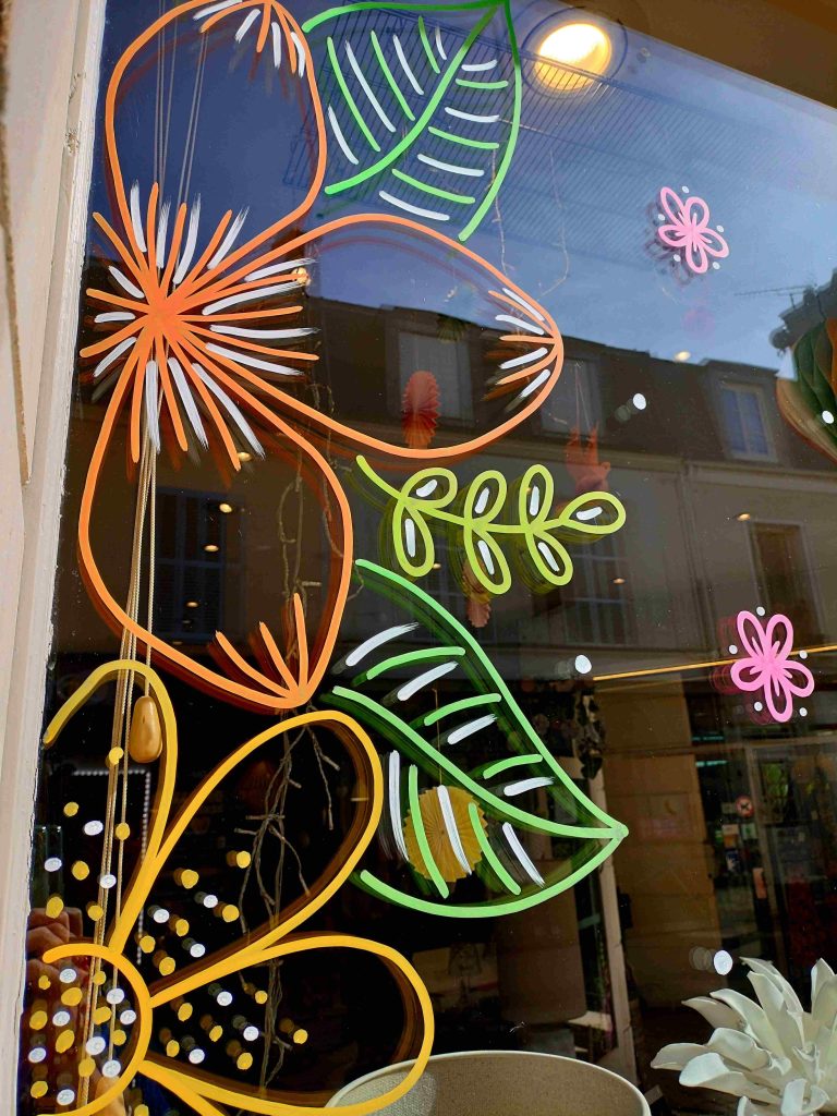 Peinture sur vitrine réalisée à Rambouillet pour une boutique de déco représentant des grandes fleurs colorées modernes pour le printemps