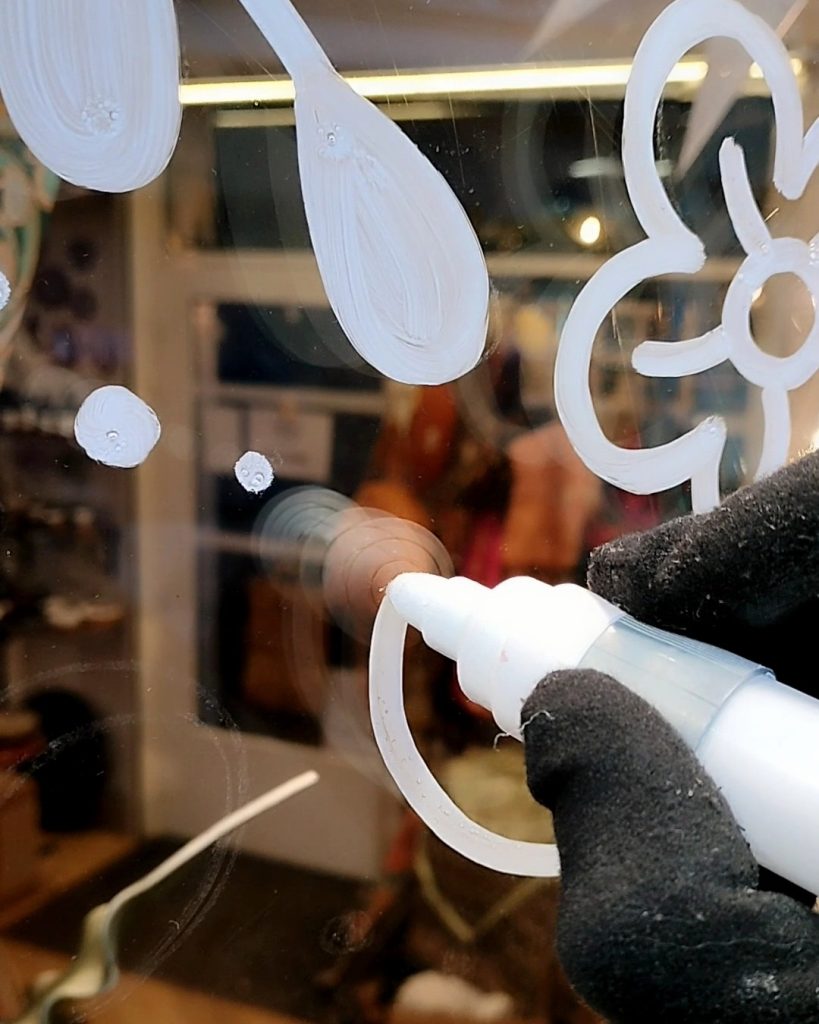 Camille Fauquet peignant un motif au feutre acrylique sur une vitrine de Noël