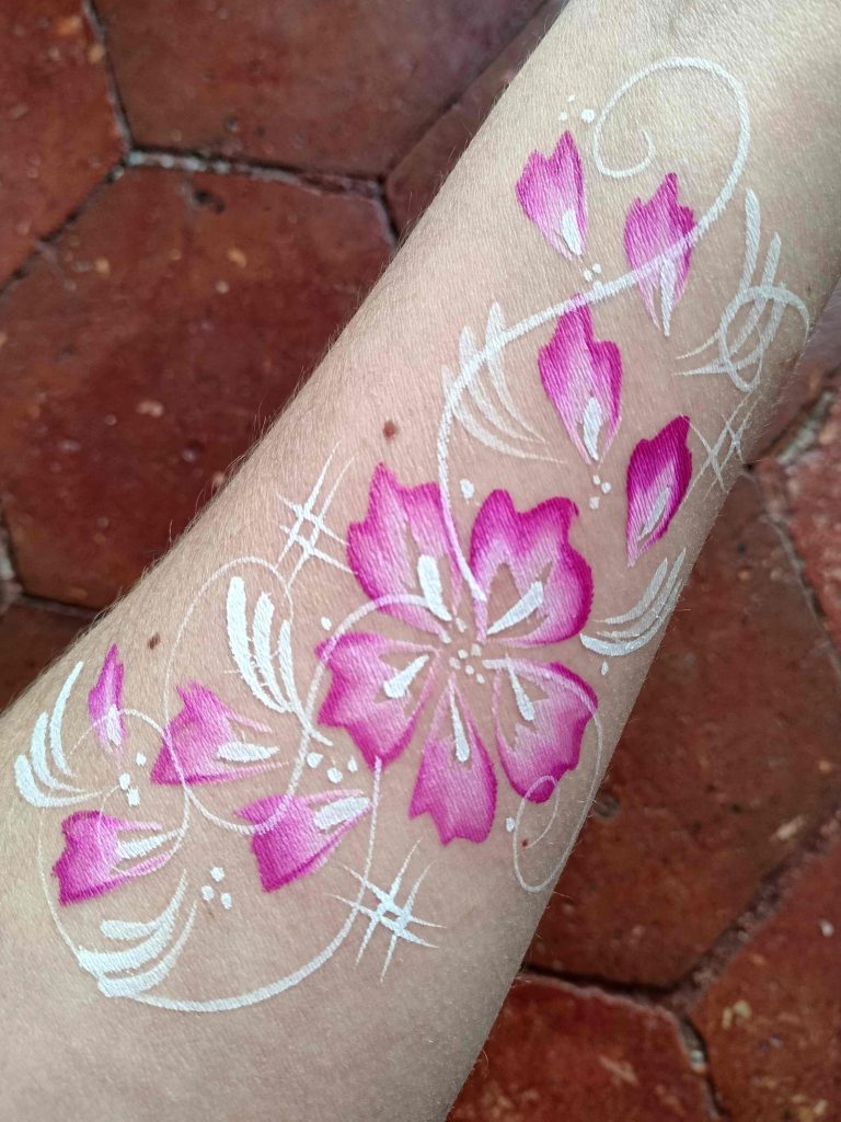 Face-painting sur le bras avec un motif de grande fleur rose et des arabesques par Camille F créations