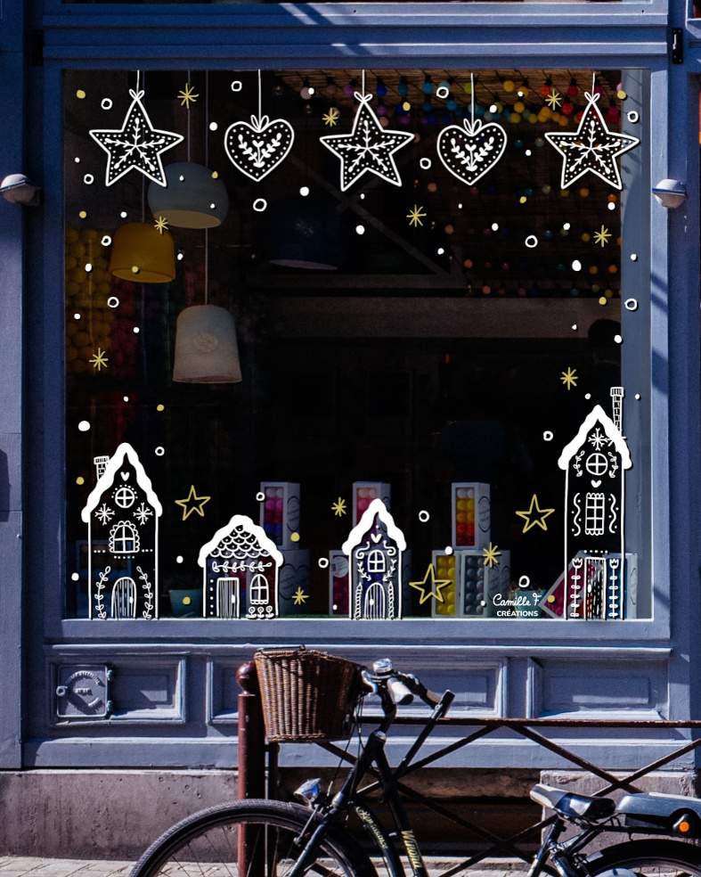 Peinture sur vitrine pour Noël représentant des maisons enneigées et des suspensions en forme d'étoiles et de cœurs.