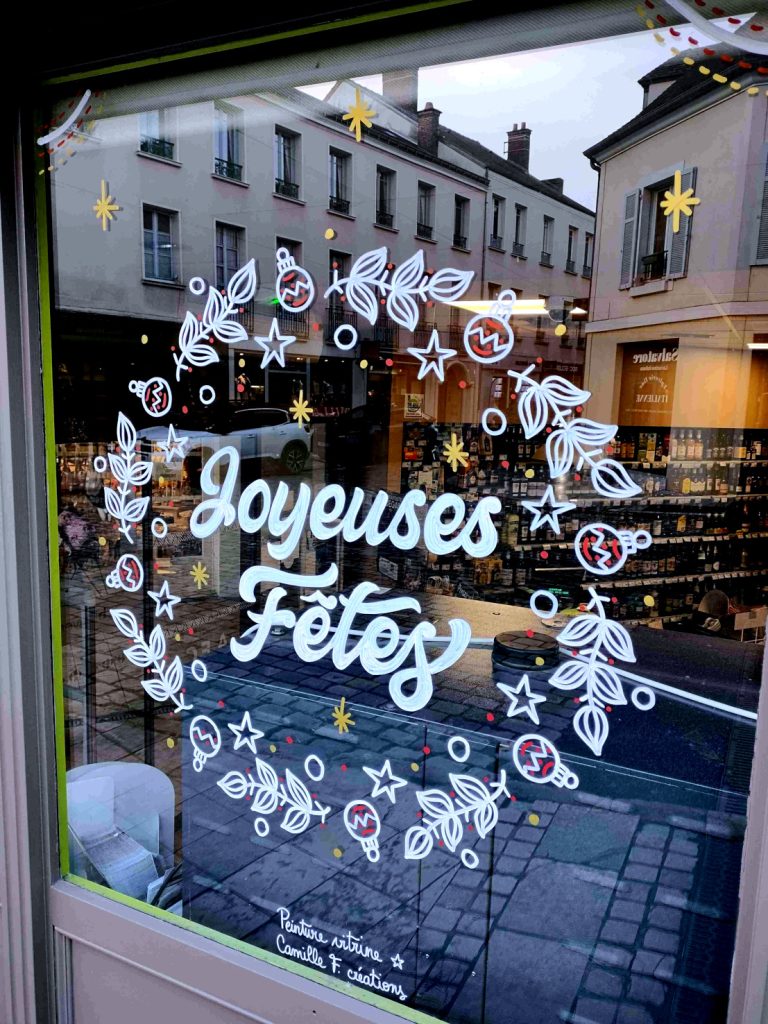 Peinture sur vitrine représentant une couronne de Noël avec l'inscription Joyeuses Fêtes à l'intérieur, par Camille F créations