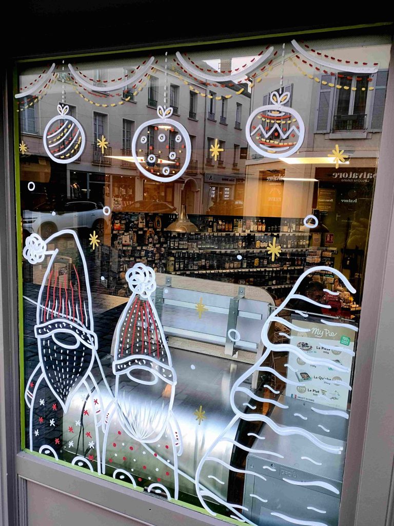 Peinture du vitrine représentant 2 sapins enneigés avec un lutin et des boules de Noël, par Camille F créations
