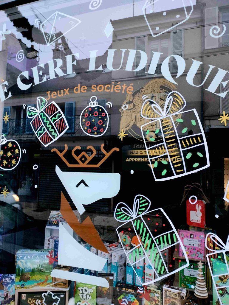 Peinture vitrine de Noël représentant des cadeaux pour la boutique de jeux de société Le Cerf Ludique à Rambouillet