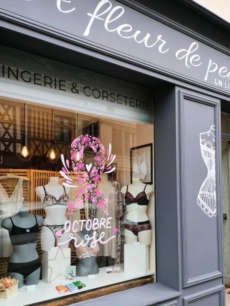 Peinture sur vitrine pour Octobre Rose représentant un ruban fleuri sur la boutique de lingerie À fleur de peau